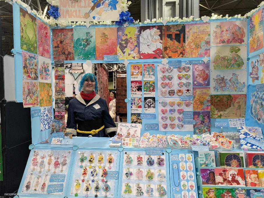 One of the stalls in artist alley with the artist wearing a Pokémon Legends cosplay